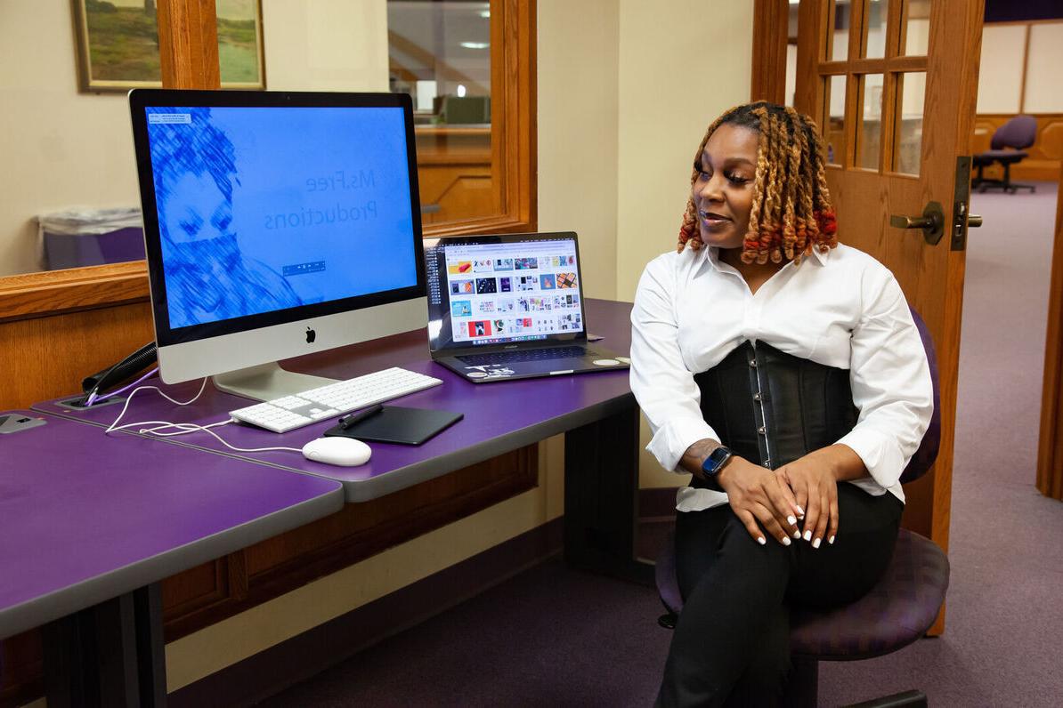 A female student looks at a laptop and desktop computer she's been using to complete a project.